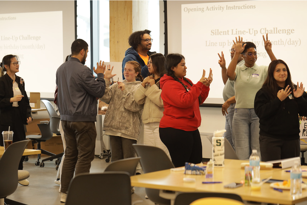 A group of students interacts in a leadership activity with their arms up